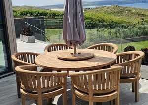 Teak dining set with a parasol, overlooking a green landscape and blue skies.