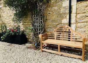 A teak garden bench beside a stone wall, with gravel and potted plants nearby.