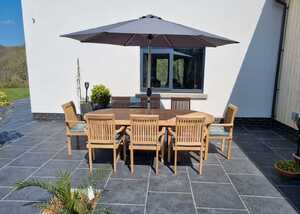 Teak outdoor dining set with a large parasol on a patio beside a house.