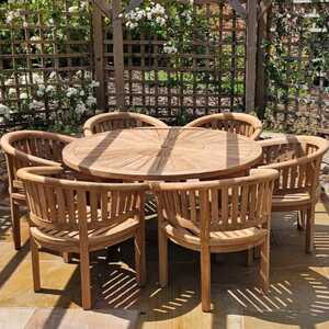 A round teak dining table surrounded by six teak chairs in a garden setting.