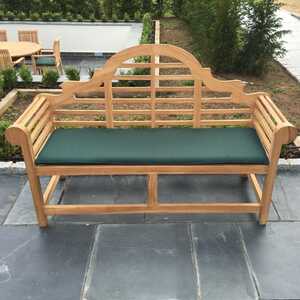 Teak garden bench with a green cushion, set outdoors among garden features.