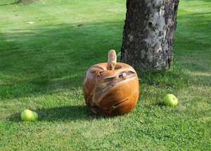 A large, carved wooden apple ornament sits on green grass next to two apples.