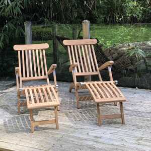 Two teak loungers on a wooden deck in a garden setting.